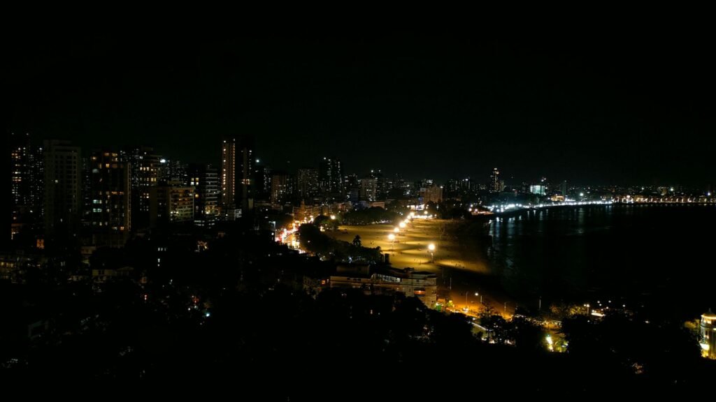 The Mumbai coastline at night, the curve of the shore picked out by street lamps with apartment towers glowing against a dark sky.